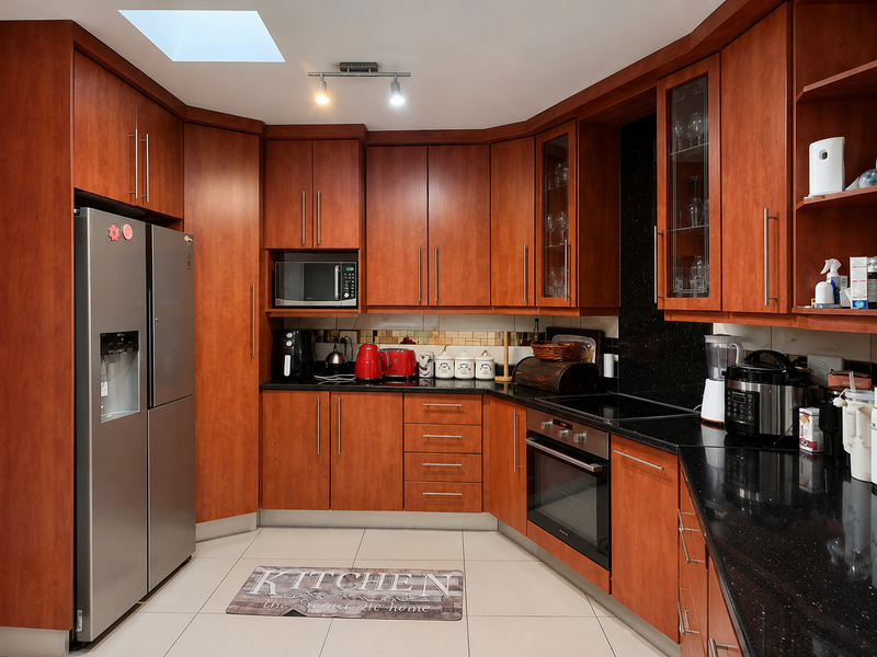 A well-maintained kitchen featuring warm-toned wooden cabinetry, black granite countertops, integrated appliances, and a skylight providing natural illumination.