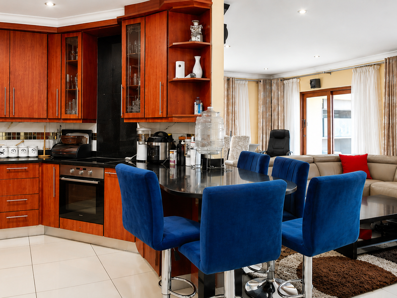Open-plan kitchen and living area featuring warm-toned wooden cabinetry, granite countertops, integrated appliances, and polished floor tiles, creating a functional and cohesive living space.