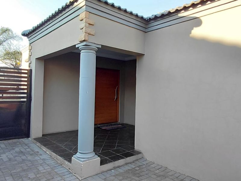 Front entrance area featuring a covered porch with a decorative column, stone detailing, and a paved driveway with a secure metal gate.