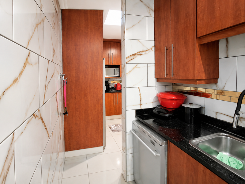 A functional scullery featuring wood-finish cabinetry, black granite countertops, stainless steel sink, and modern marble-look wall tiling.