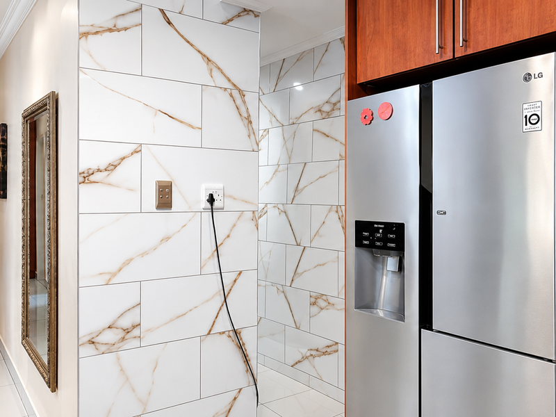 A well-maintained hallway featuring marble-effect wall tiles, built-in wooden cabinetry, and recessed ceiling lighting, creating a clean and modern transition space.