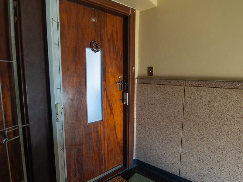 Apartment entrance featuring a wooden door with a frosted glass panel and granite wall cladding in the hallway.