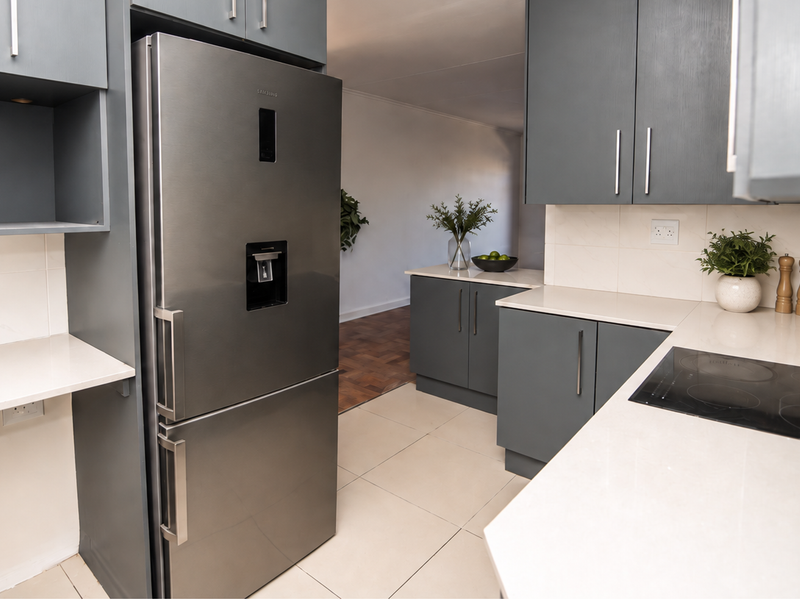 Modern kitchen featuring dark grey cabinetry, light quartz countertops, integrated induction hob, and sleek tiled flooring in a well-maintained apartment setting.