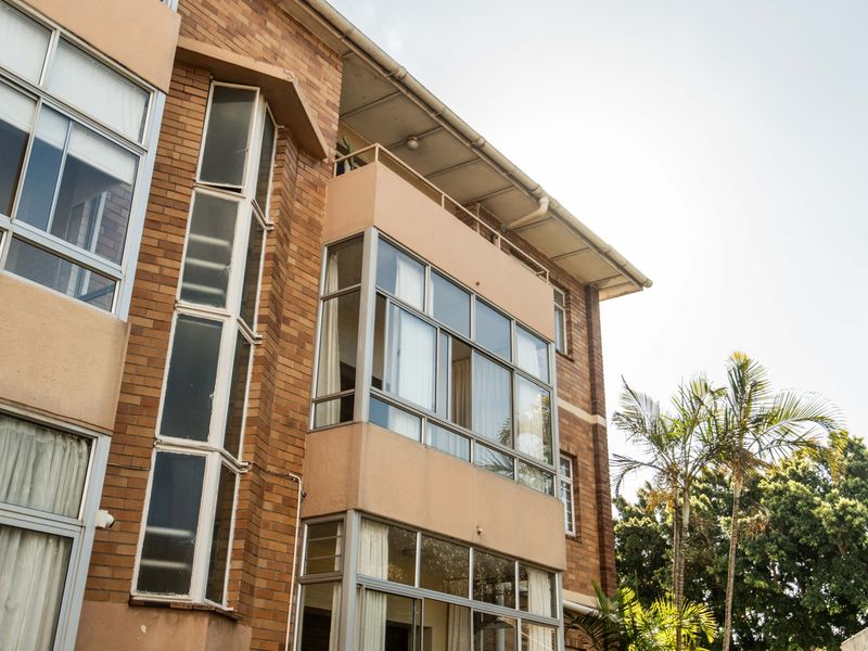 Exterior view of a multi-story apartment building featuring brick cladding, large aluminium-framed windows, and a private balcony.
