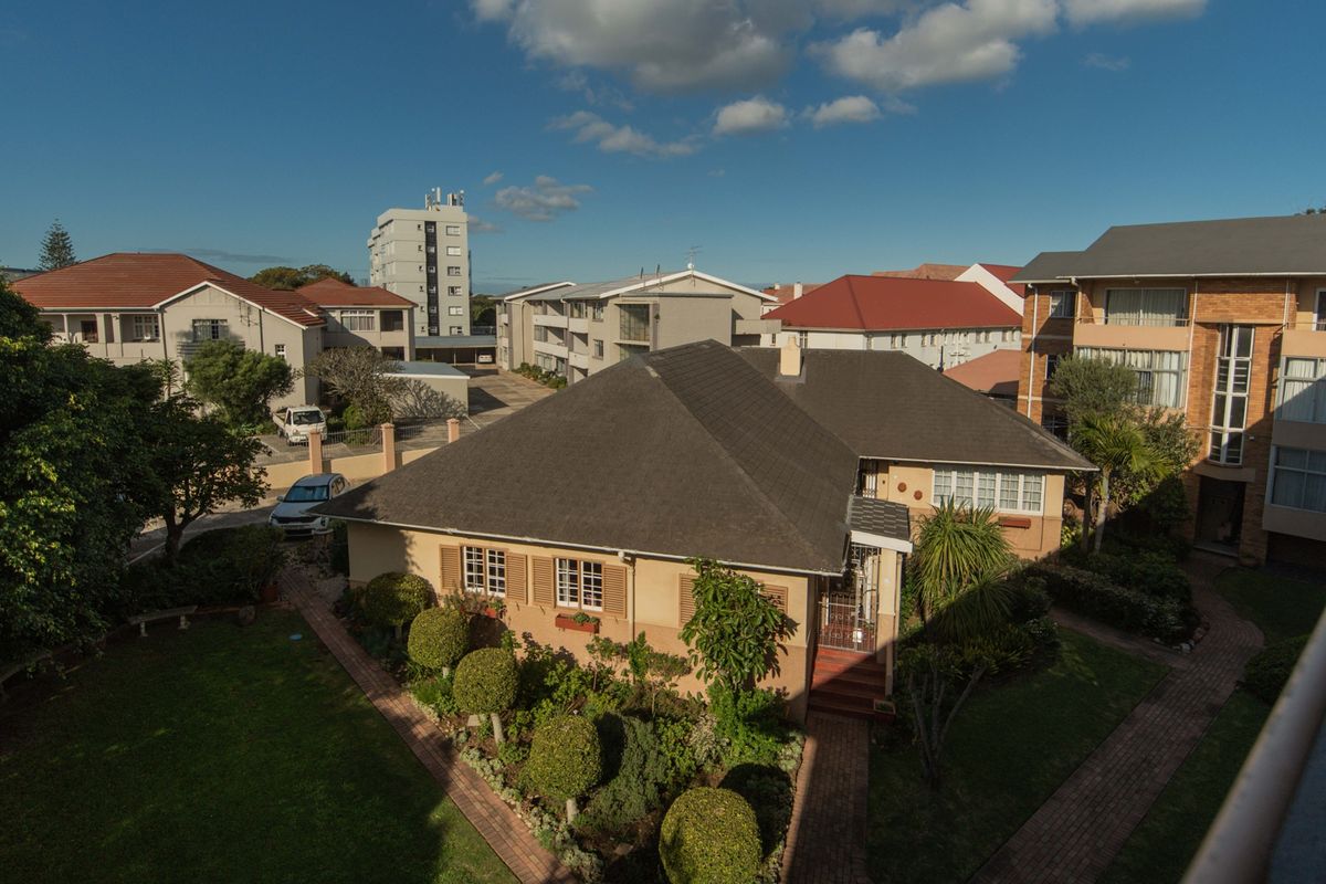 An elevated aerial view of the apartment complex grounds, featuring well-maintained gardens, paved pathways, and surrounding residential buildings.