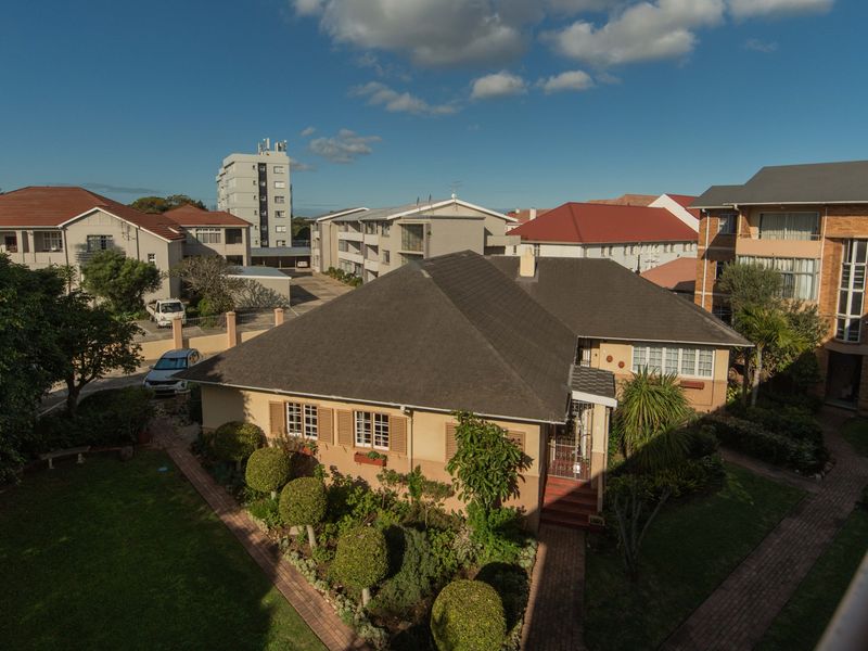 An elevated aerial view of the apartment complex grounds, featuring well-maintained gardens, paved pathways, and surrounding residential buildings.