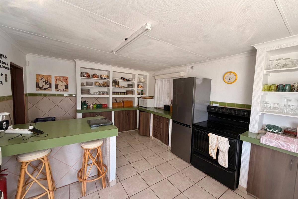 A functional kitchen featuring built-in cabinetry, open shelving, a breakfast bar, and tiled flooring, offering a practical layout with potential for modern updates.