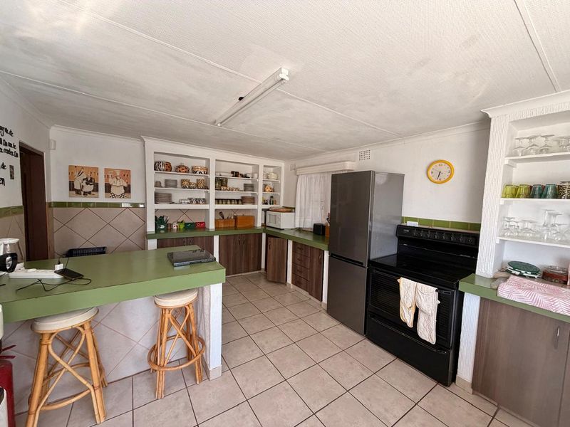 A functional kitchen featuring built-in cabinetry, open shelving, a breakfast bar, and tiled flooring, offering a practical layout with potential for modern updates.