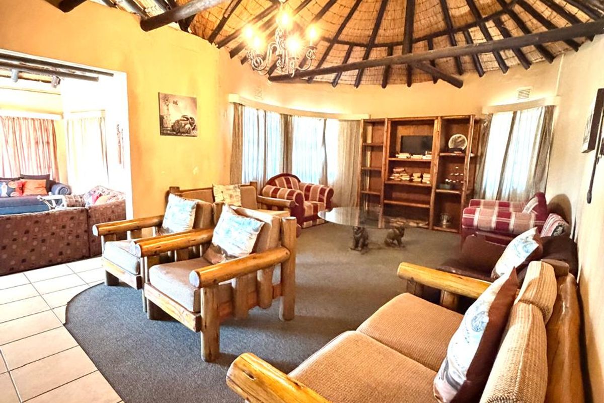 Spacious living room featuring a traditional thatched roof with exposed timber rafters, built-in shelving, and a combination of tiled and carpeted flooring.