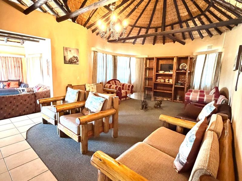 Spacious living room featuring a traditional thatched roof with exposed timber rafters, built-in shelving, and a combination of tiled and carpeted flooring.