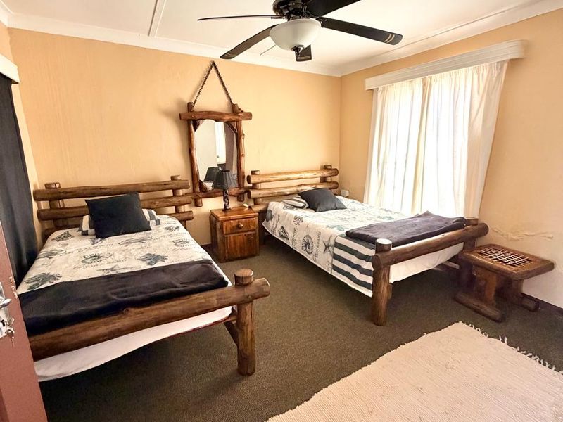 A bedroom featuring carpet flooring and a ceiling fan, with visible water staining on the wall near the window area.