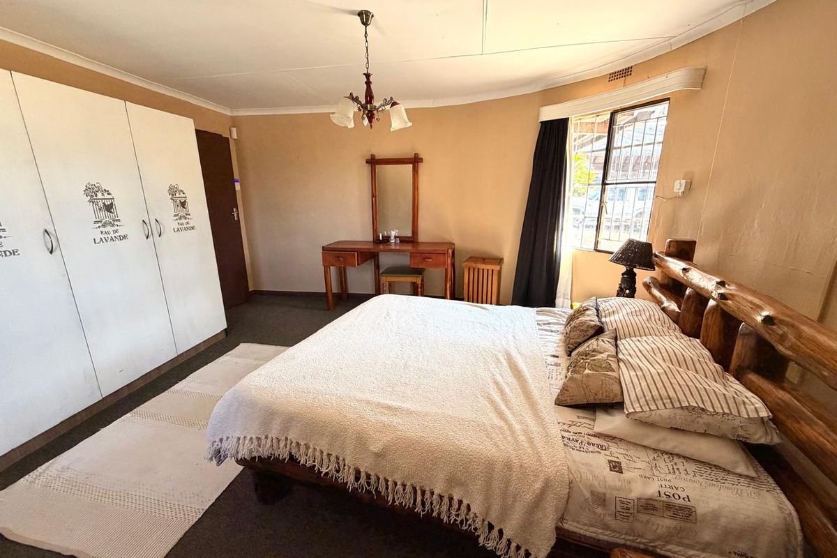A spacious bedroom featuring built-in cupboards, a ceiling light fixture, and a window with security bars, offering a functional layout for a farm property.