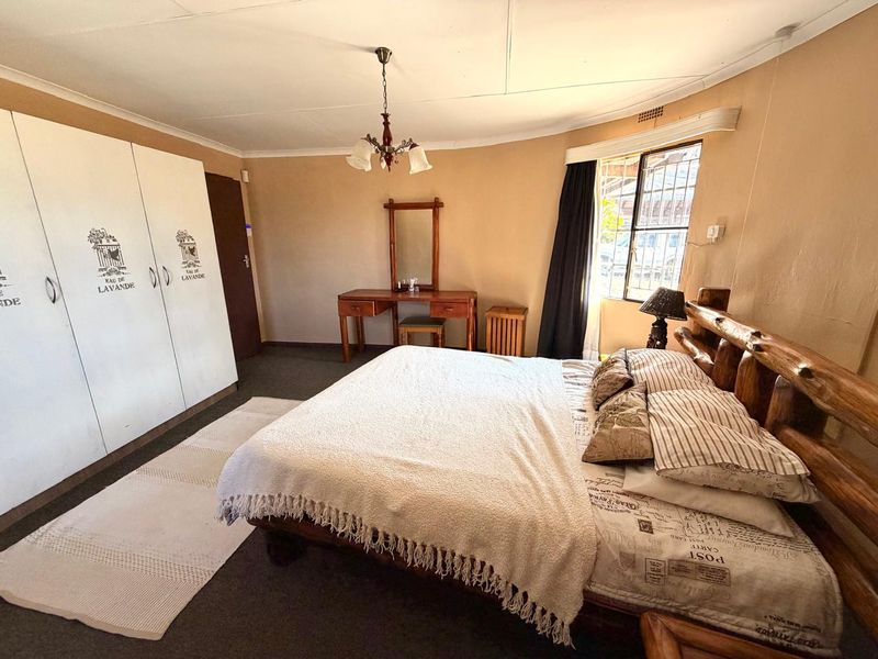 A spacious bedroom featuring built-in cupboards, a ceiling light fixture, and a window with security bars, offering a functional layout for a farm property.