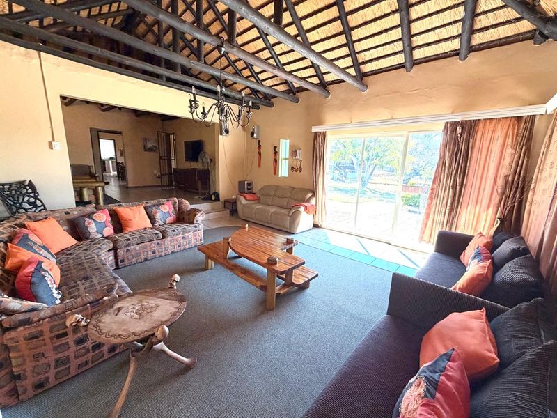 Spacious living room featuring a high thatched ceiling with exposed timber trusses, tiled flooring, and large sliding glass doors providing natural light.