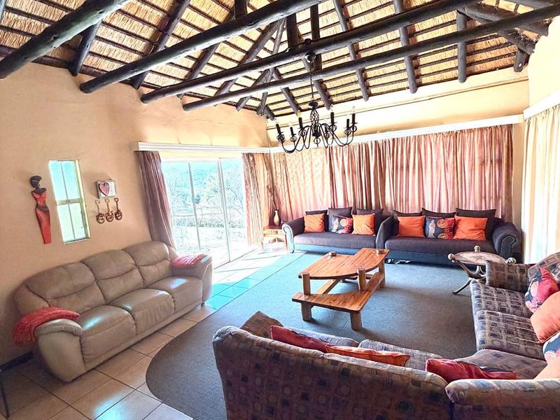 Spacious living room featuring a high vaulted thatched ceiling with exposed timber rafters, tiled flooring, and large sliding doors leading to the outdoors.