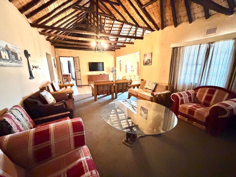 Spacious living room featuring a traditional exposed timber thatch roof and tiled flooring, offering a rustic atmosphere with potential for modern updates.