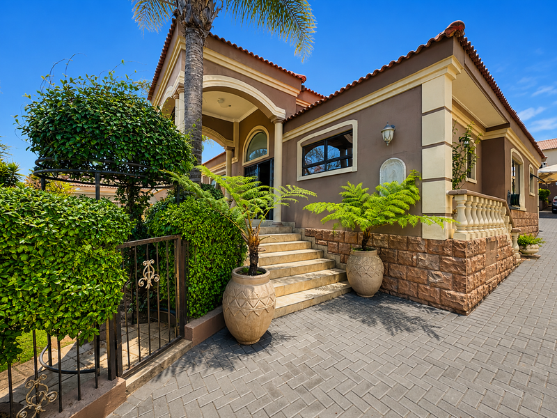Front entrance of a Mediterranean-style house featuring stone cladding, a paved driveway, and an arched entryway with decorative columns.