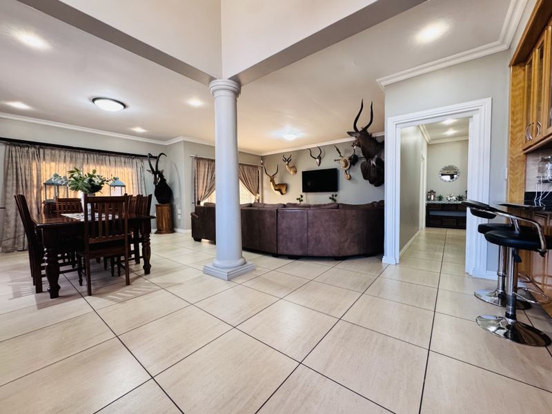Spacious open-plan living and dining area featuring neutral tiled flooring, a central structural column, and integrated kitchen cabinetry with breakfast bar seating.