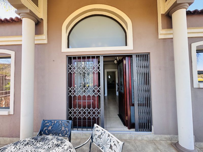 Main entrance featuring a wooden door with a security gate, arched transom window, and covered patio area with structural columns.
