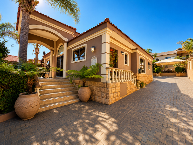A well-maintained Mediterranean-style home featuring stone cladding, a paved driveway, and a covered entrance with a decorative balustrade.