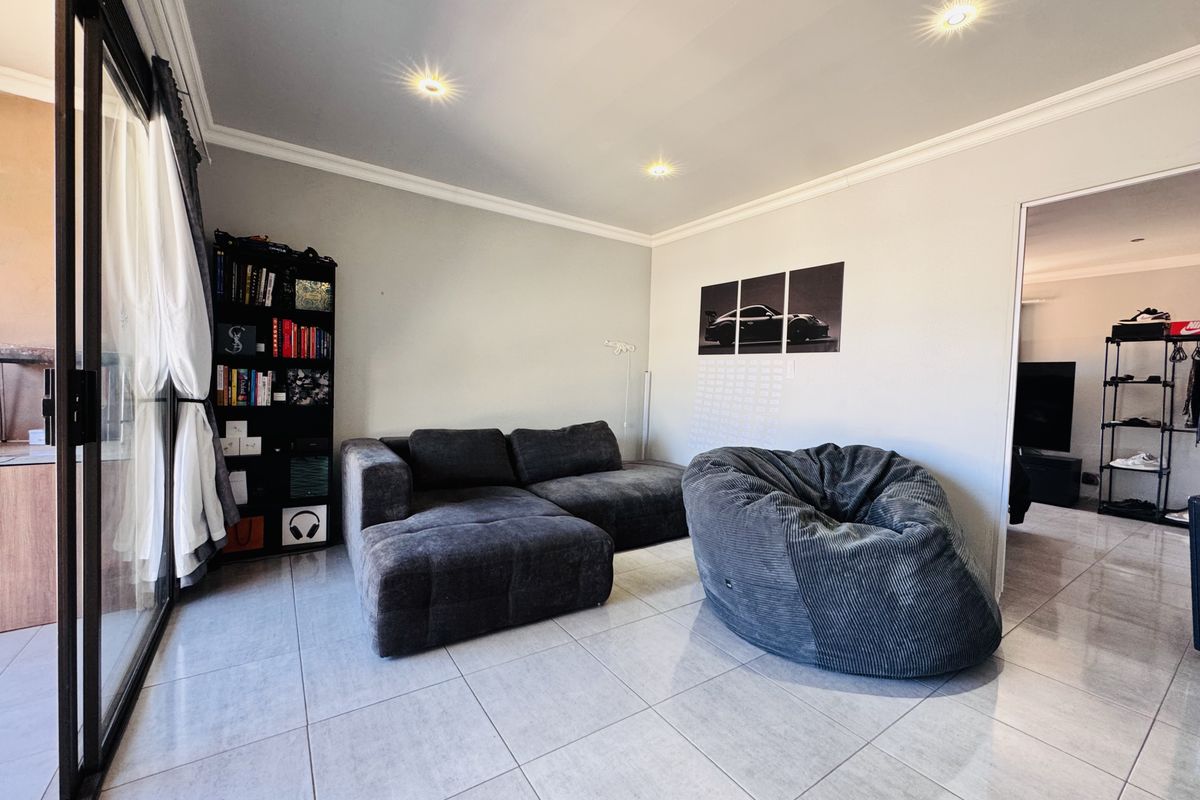 A modern living room featuring large format floor tiles, recessed downlighting, and a sliding glass door providing access to the outdoor area.
