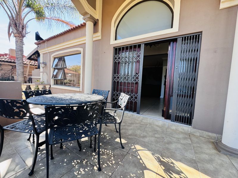 A covered patio area featuring tiled flooring, decorative columns, and a secure metal gate leading into the main living space.