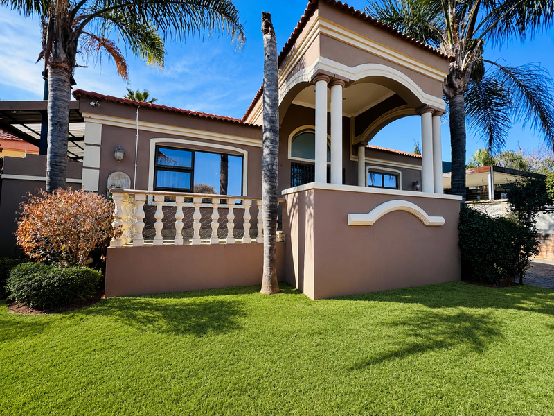 Front elevation of a house featuring a covered porch with decorative columns, a balustrade, and terracotta roof tiles set against a landscaped lawn.