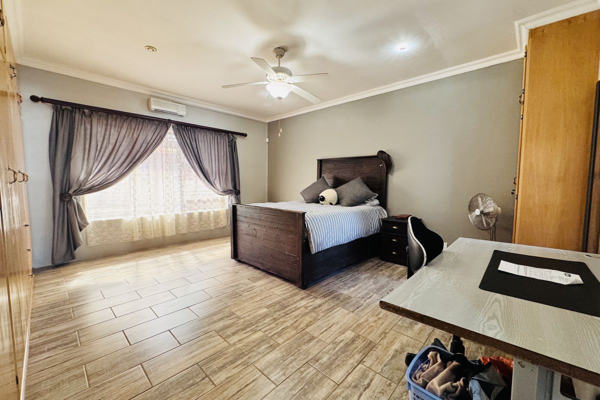 Spacious bedroom featuring tiled flooring, built-in cupboards, coved cornicing, and a ceiling fan with an integrated air conditioning unit.