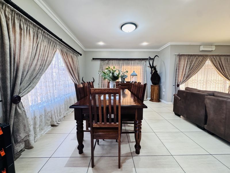 Spacious dining room featuring neutral tiled flooring, wall-mounted air conditioning, and large windows with curtain rails, offering a bright and functional living space.