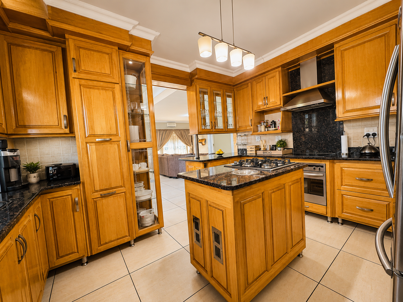 A well-maintained kitchen featuring warm wooden cabinetry, granite countertops, a central island with a gas hob, and integrated appliances.