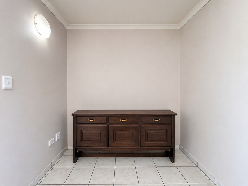 A neutral, tiled alcove or transition space featuring a wall-mounted light fixture and electrical points, suitable for various functional uses.