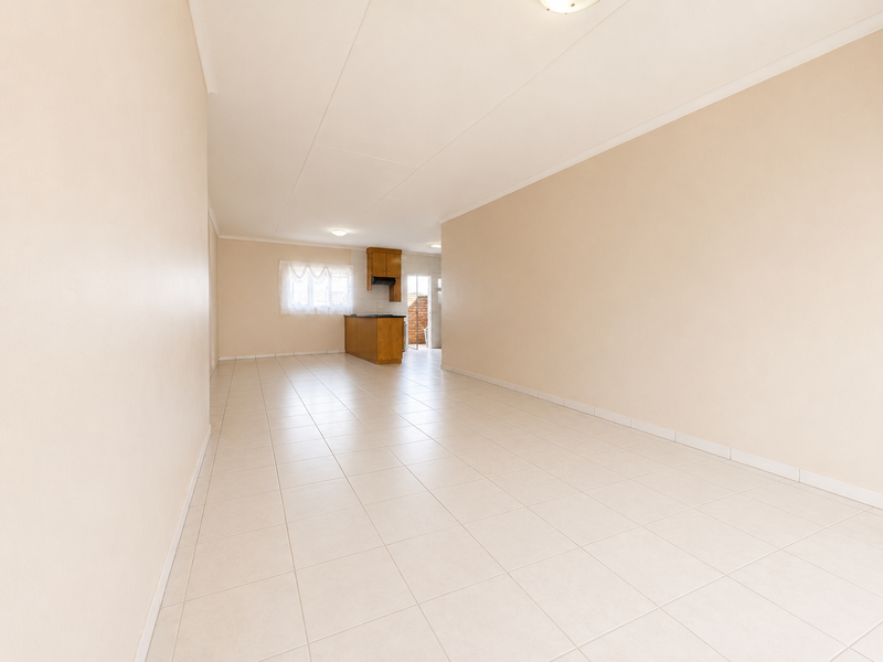 A spacious, empty open-plan living and kitchen area featuring neutral tiled flooring and simple cabinetry, offering a blank canvas for interior design.