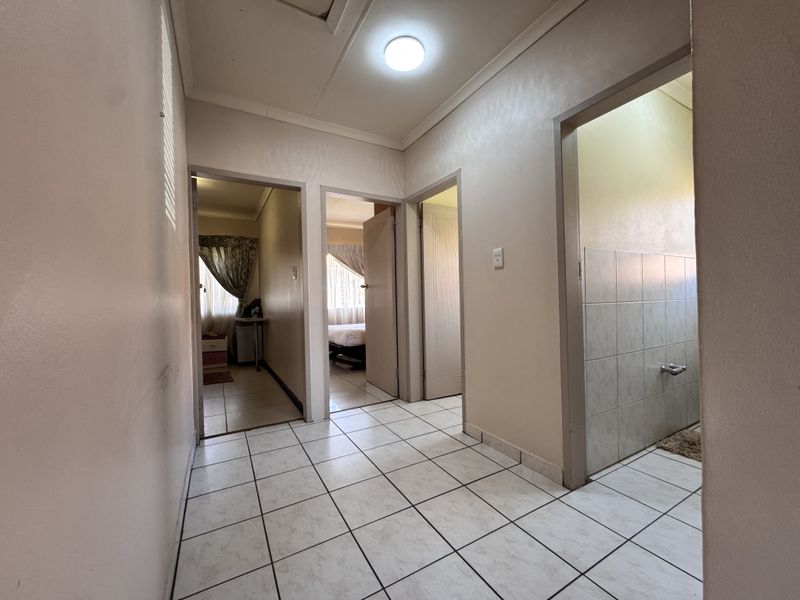 A functional tiled hallway providing access to multiple rooms, featuring neutral wall finishes and standard ceiling lighting.