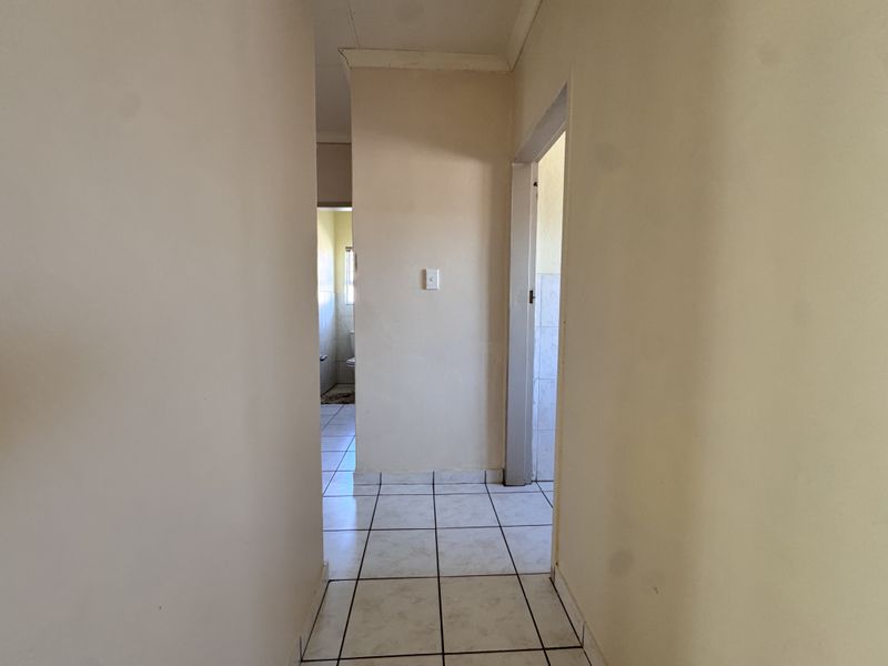 A narrow hallway with ceramic floor tiles leading to adjacent rooms, featuring plain walls and standard door frames.
