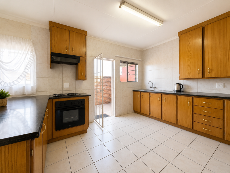 A functional kitchen featuring wooden cabinetry, laminate countertops, built-in oven, and tiled flooring with direct access to an outdoor area.