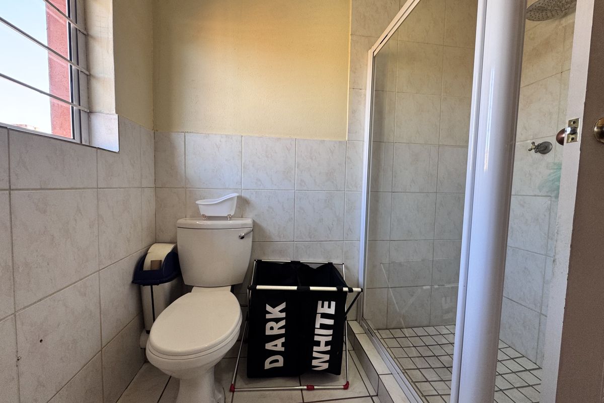 A functional bathroom featuring a shower enclosure, toilet, and tiled finishes, offering a practical layout with natural light from the side window.
