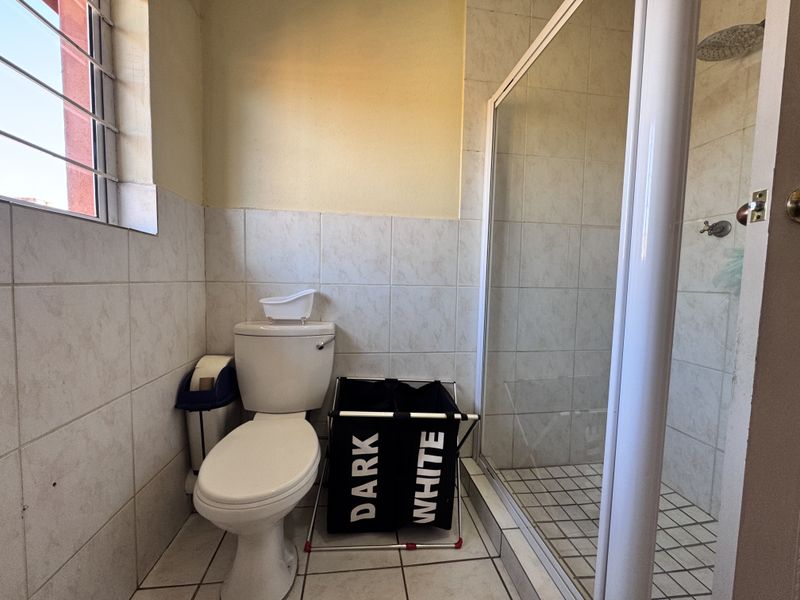 A functional bathroom featuring a shower enclosure, toilet, and tiled finishes, offering a practical layout with natural light from the side window.