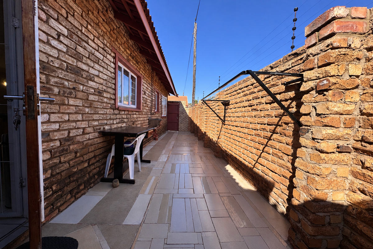 A narrow rear exterior walkway featuring face brick walls, tiled flooring, and a wall-mounted washing line, enclosed by a brick boundary wall with electric fencing.
