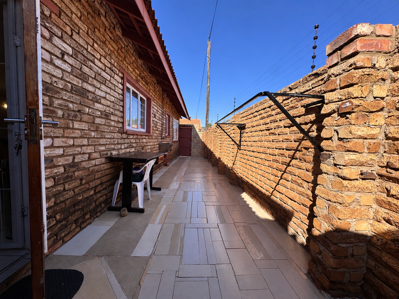 A narrow rear exterior walkway featuring face brick walls, tiled flooring, and a wall-mounted washing line, enclosed by a brick boundary wall with electric fencing.