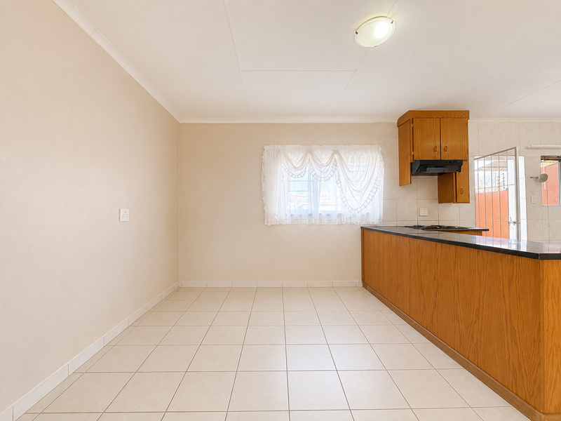 Open plan kitchen and dining area featuring tiled flooring, wooden cabinetry, and a black granite countertop with a built-in hob and extractor fan.