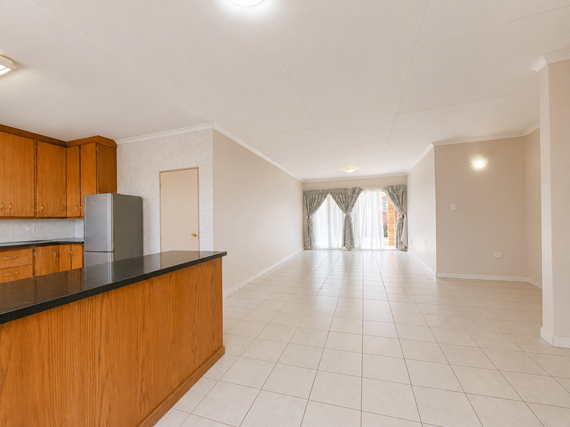 Spacious open-plan living and kitchen area featuring tiled flooring, wooden cabinetry with granite countertops, and sliding doors leading to the exterior.