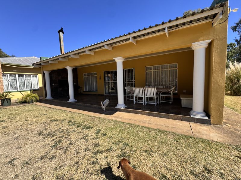 A spacious covered patio featuring tiled flooring, structural columns, and a built-in fireplace, providing an ideal outdoor entertainment area overlooking the garden.