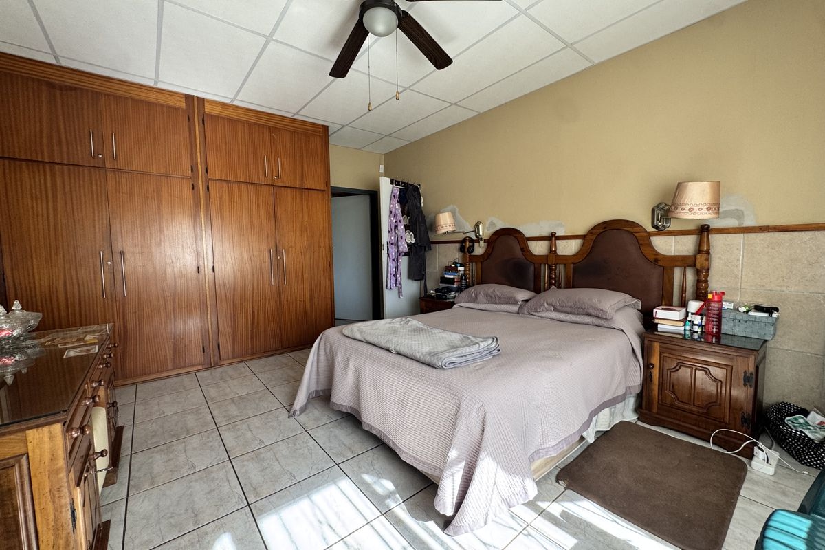 Spacious bedroom featuring built-in wooden cupboards, tiled flooring, and a ceiling fan, requiring some cosmetic wall repairs.