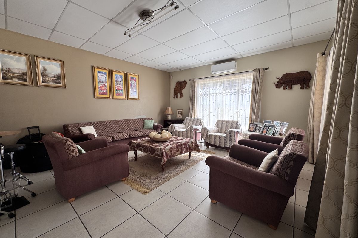 A spacious living room featuring tiled flooring, a drop ceiling, and a wall-mounted air conditioning unit, providing a comfortable and functional living space.