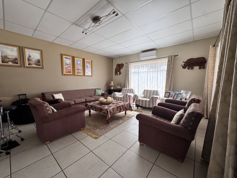 A spacious living room featuring tiled flooring, a drop ceiling, and a wall-mounted air conditioning unit, providing a comfortable and functional living space.