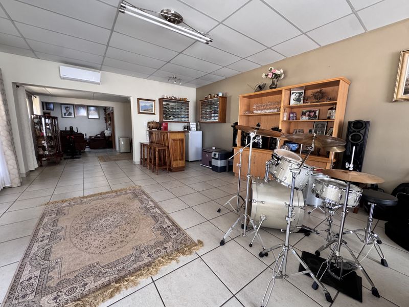 Spacious entertainment area featuring a built-in bar, tiled flooring, and a suspended ceiling, currently utilized as a multi-purpose living and music space.