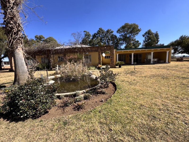 Rear view of the small holding featuring a brick facade, covered patio with decorative columns, and a landscaped garden with a central pond.