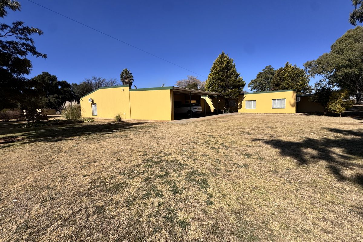 Rear view of the property featuring a yellow facade, integrated carport, and expansive surrounding garden area.