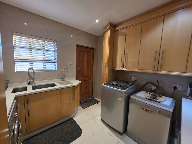 A functional laundry room featuring wooden cabinetry, stone countertops, a double sink, and tiled finishes, providing ample storage and workspace for utility tasks.