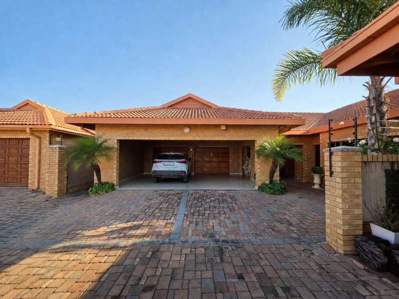 Front elevation of a townhouse featuring a paved driveway, face brick facade, tiled roof, and a spacious double garage with covered parking.